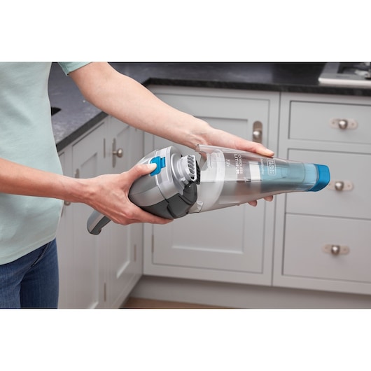 BLACKDECKER NVC215WA handheld vacuum cleaner with blue nozzle held in kitchen.