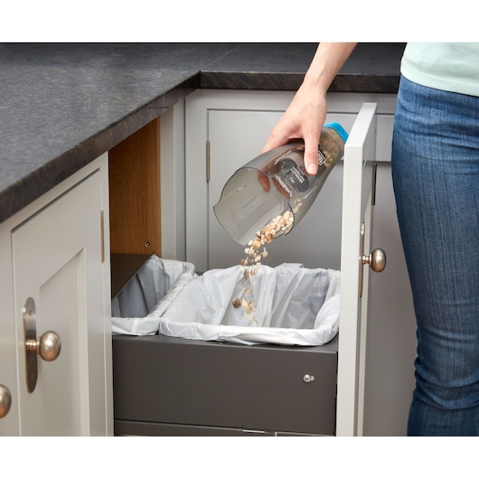 BLACKDECKER NVC215WA handheld vacuum being emptied into kitchen trash bin, angled view.