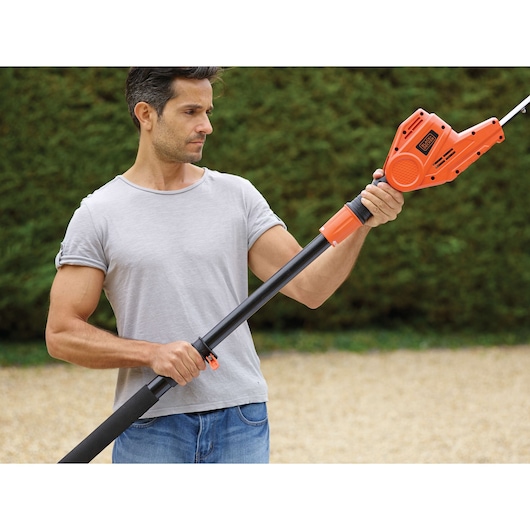 BLACKDECKER PH5551 pole hedge trimmer held by person outdoors, showing orange and black tool body and telescopic handle.
