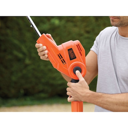 Close-up photo of a person adjusting BLACK+DECKER PH5551 orange hedge trimmer handle outdoors.