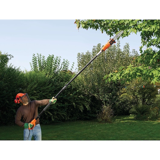 Photo of BLACK+DECKER PS7525 pole saw being used outdoors to trim high tree branches.