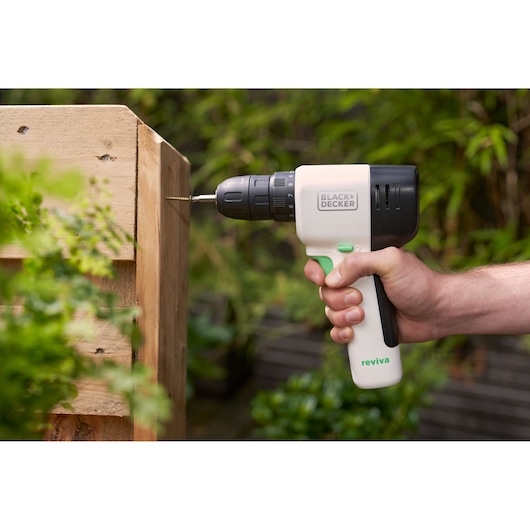 BLACK+DECKER REVDD12C cordless drill driving screw into wooden board outdoors.