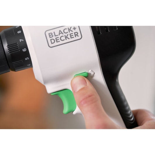 Close-up photo of BLACK+DECKER REVDD12C cordless drill, green trigger and side button pressed by a hand.