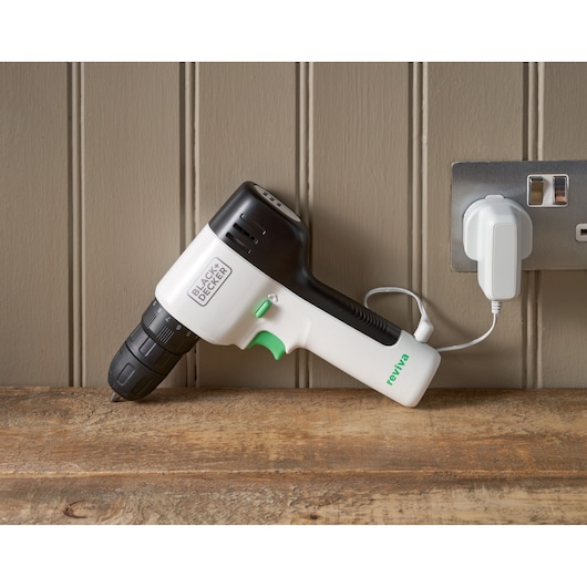 BLACK+DECKER REVDD12C cordless drill with black and white body, green accents, charging on a wooden surface.