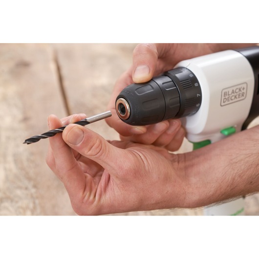 Photo of hands inserting drill bit into BLACK+DECKER REVDD12C cordless drill on wooden surface.