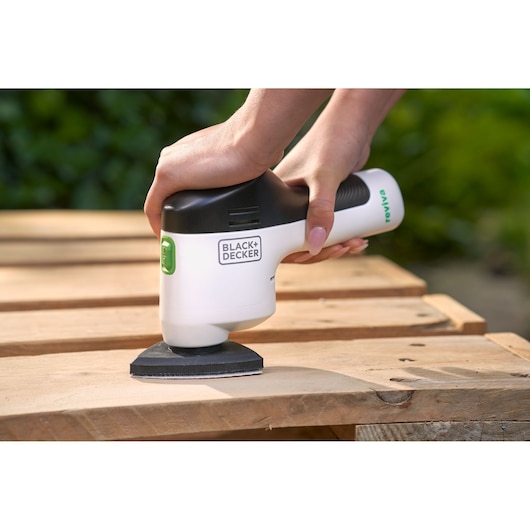 BLACK+DECKER REVDS12C cordless detail sander in use on wooden surface, hand-held, outdoor setting.