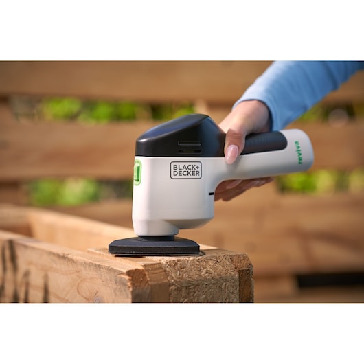 BLACK+DECKER REVDS12C handheld sander in use on wood outdoors, product held in hand.