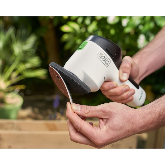 Photo of BLACK+DECKER REVDS12C detail sander held in hand, sandpaper being attached to sanding pad.