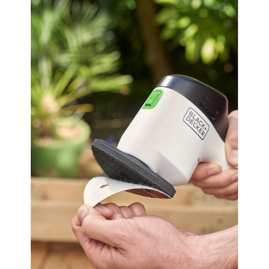 BLACK+DECKER REVDS12C handheld sander with sanding pad in a garden setting.