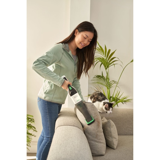 BLACKDECKER REVHV8C handheld vacuum cleaning sofa, person using appliance near cushions and cat.