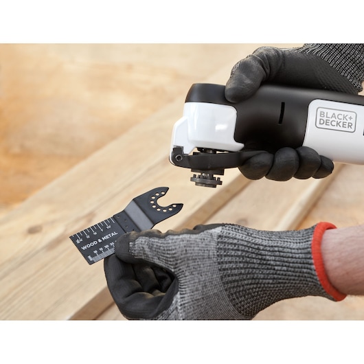Photo of BLACK+DECKER REVOS12C multi-tool being fitted with a wood and metal blade, gloved hands visible.