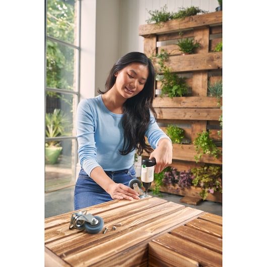 BLACKDECKER REVSD4C cordless screwdriver used to attach caster to wooden furniture indoors.
