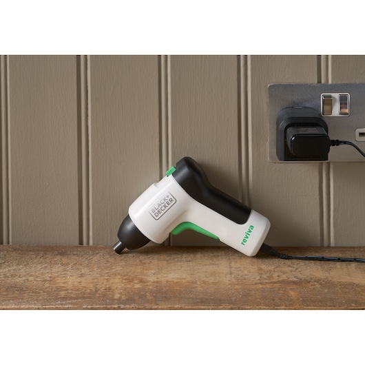 BLACK+DECKER REVSD4C cordless screwdriver in white and black charging on a wooden surface, side view.