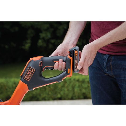 BLACK+DECKER STC1820EPC cordless trimmer handle close-up with person inserting 18V lithium battery.