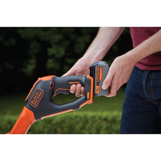 Photo of BLACKDECKER STC1840EPC trimmer handle with 18V lithium battery being inserted outdoors.