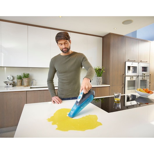 BLACK+DECKER WDA320J handheld vacuum cleaner cleaning liquid spill on kitchen counter.