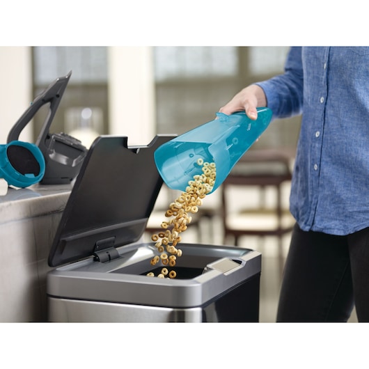 Photo of BLACKDECKER WDA320J handheld vacuum canister being emptied into a trash bin in a kitchen.
