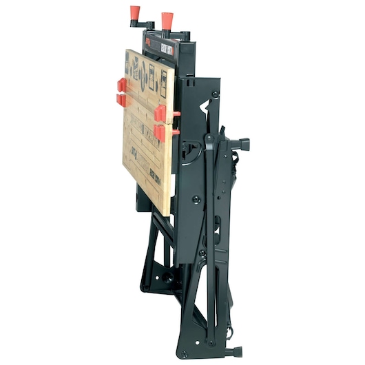 A BLACK+DECKER folding workbench, model WM825, shown in a closed and upright position. The workbench has a sturdy black metal frame and wooden surface with red clamps.